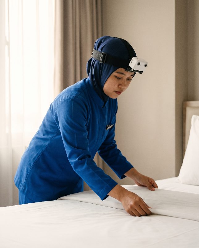 Hotel room attendant smoothing a duvet while wearing a head-mounted stereo camera